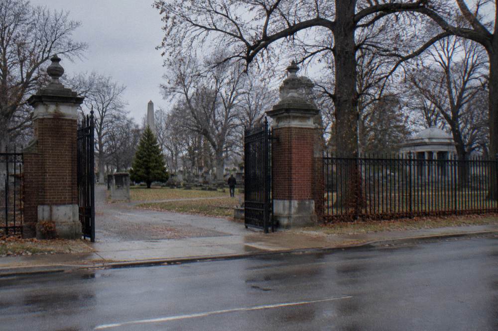 An old city cemetery gate of stone and iron with bare trees on an overcast afternoon