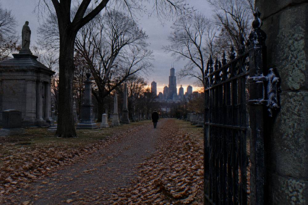 An autumn path through a historic Chicago cemetery with mature trees and old stone monuments.